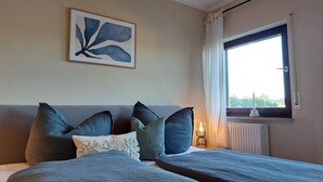 A bedroom with a bed, pillows, a radiator, a window with curtains, and a wall-mounted artwork. - Sun-drenched, family-friendly apartment with balcony & large kitchen (Bad Camberg)