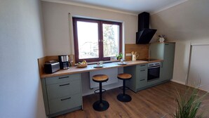 A compact kitchen with a window, a stove, and two stools. - Sun-drenched, family-friendly apartment with balcony & large kitchen (Bad Camberg)
