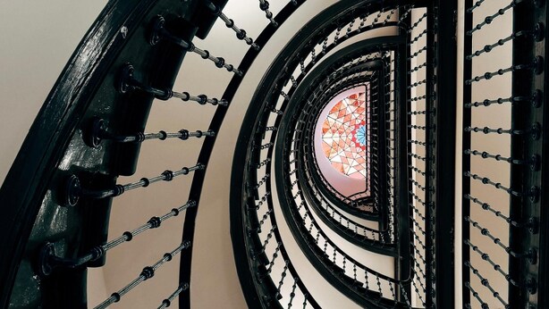 A spiral staircase with black railings and a geometric stained glass window at the top. - Adventure Hostel Madrid Gran vía (Madrid)