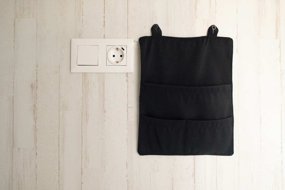 A black bag with multiple pockets, a white electrical outlet, and a wooden wall.