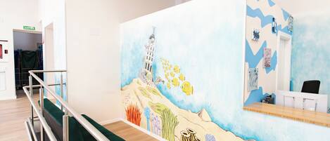A room with a mural of a beach scene, a bed with green bedding, a desk with a computer, and a chair.