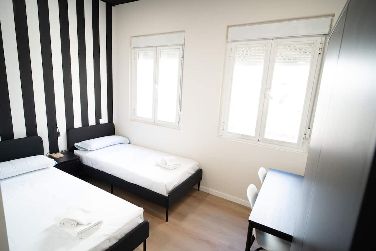Ein Zimmer mit zwei Betten, einem Schreibtisch und zwei Fenstern mit Fensterläden.