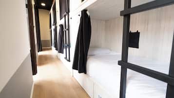 Un pasillo estrecho con literas a ambos lados, suelo de madera y cortinas negras.