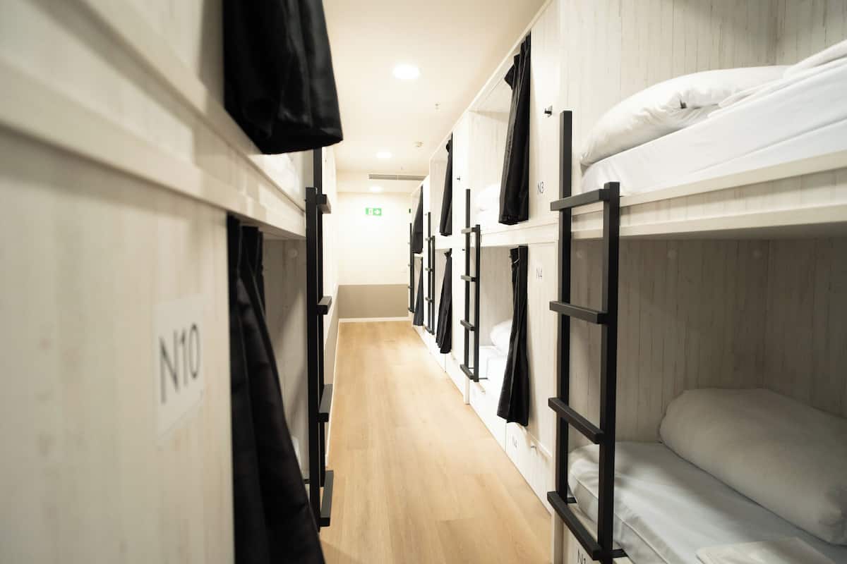 Ein Korridor mit Stockbetten, beschriftet mit N10, N11 und N12, Holzboden und einer weißen Wand.