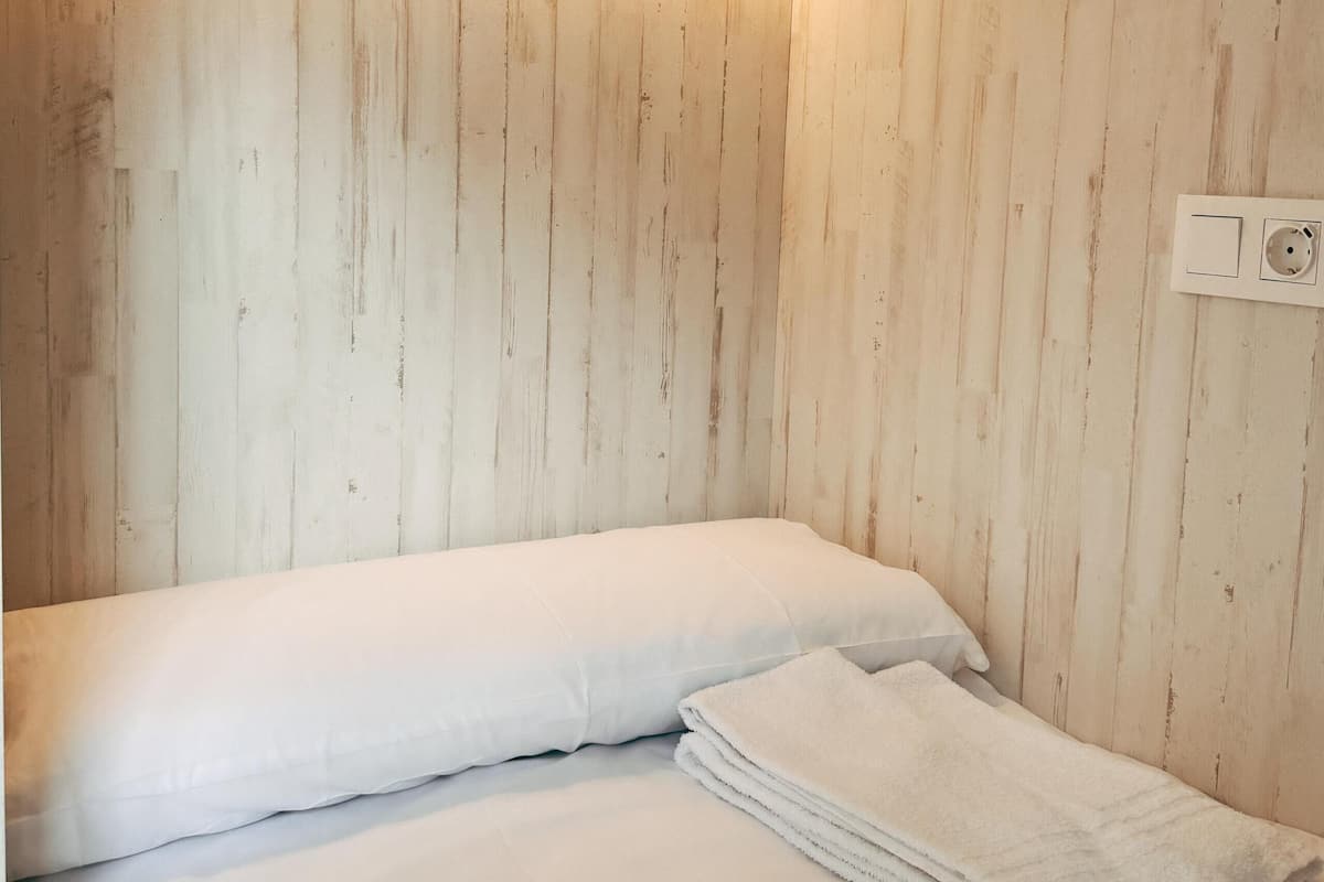 Ein Zimmer mit Holzwänden, einem Bett mit weißen Leinen und einer wandmontierten Lampe.