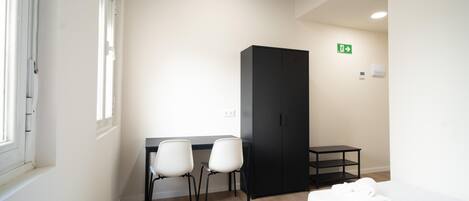 A hotel room with a bed, two chairs, a desk, a wardrobe, and a small table.
