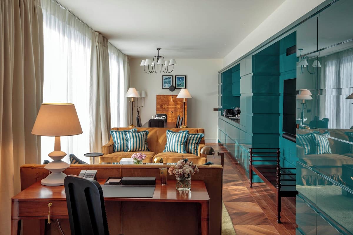 A modern living room with a wooden herringbone floor, a sofa set with blue and white striped pillows, a dining area with a wooden table and chairs, and a teal accent wall.