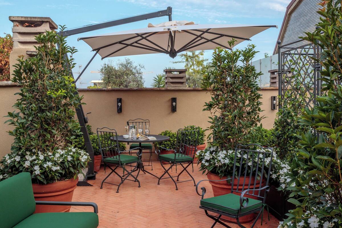 Une terrasse extérieure avec un sol en terre cuite, des chaises rembourrées vertes et des plantes en pot.