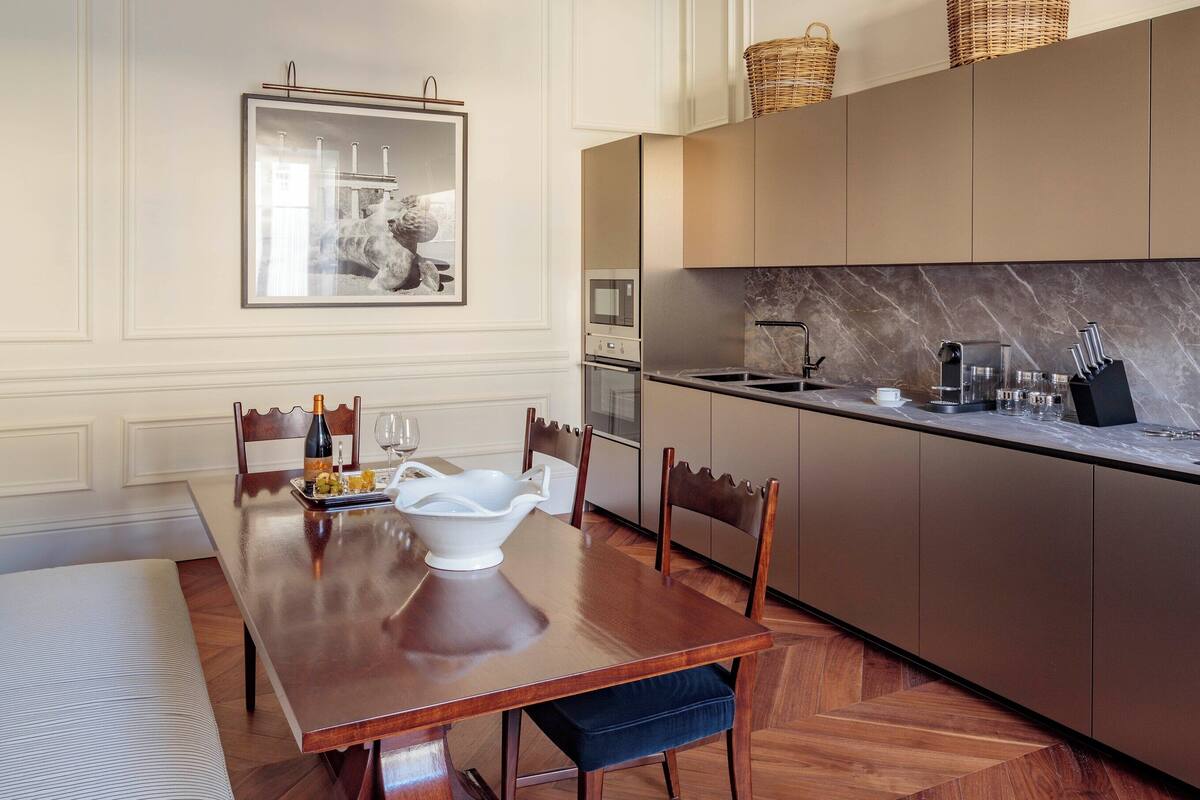 Un coin repas avec une table en bois, des chaises et un lustre. Il y a également un coin cuisine avec des placards et un four à micro-ondes.