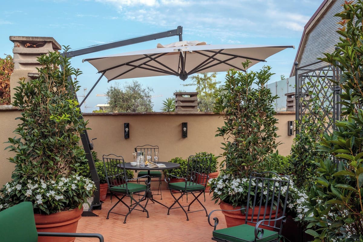 An outdoor patio with terracotta flooring, green cushioned chairs, and potted plants.
