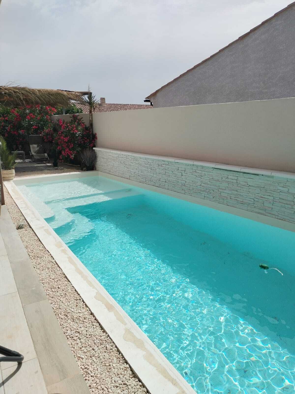 A rectangular swimming pool with clear blue water, surrounded by a stone wall and a tiled deck.