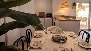 Zona pranzo con tavolo apparecchiato per quattro, cucina sullo sfondo e vista sull'esterno.