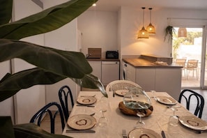Un coin repas avec une table dressée pour quatre personnes, une cuisine en arrière-plan et une vue sur l’extérieur.