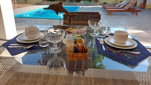 Ein Esstisch mit Blick auf einen Swimmingpool und Liegestühle im Hintergrund.