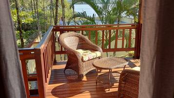Um deck de madeira com mobiliário de vime, guarda-corpo e vista para o mar e montanhas.