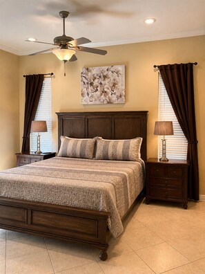 A bedroom with a wooden bed, two bedside tables, a ceiling fan, and a wall-mounted artwork.