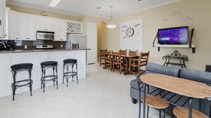 Een moderne keuken met witte kasten, een magnetron en een zithoek met houten stoelen en een grijze bank.