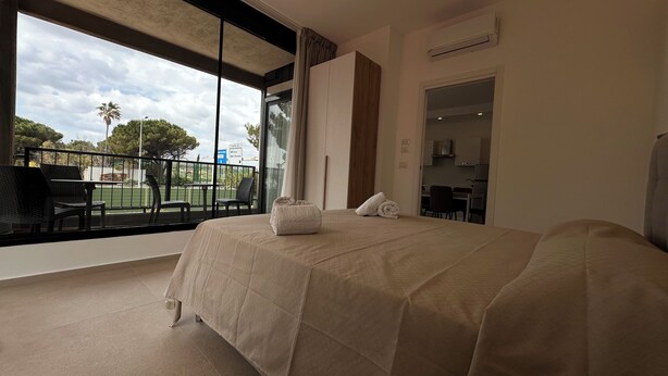 A hotel room with a large bed, a balcony with outdoor seating, and a view of the surrounding landscape. - Puglia Promenade Apartment 4 (Bari)