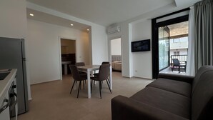 A modern living room with a sofa, a dining table with chairs, a kitchen area, and a balcony with a TV. - Puglia Promenade Apartment 4 (Bari)