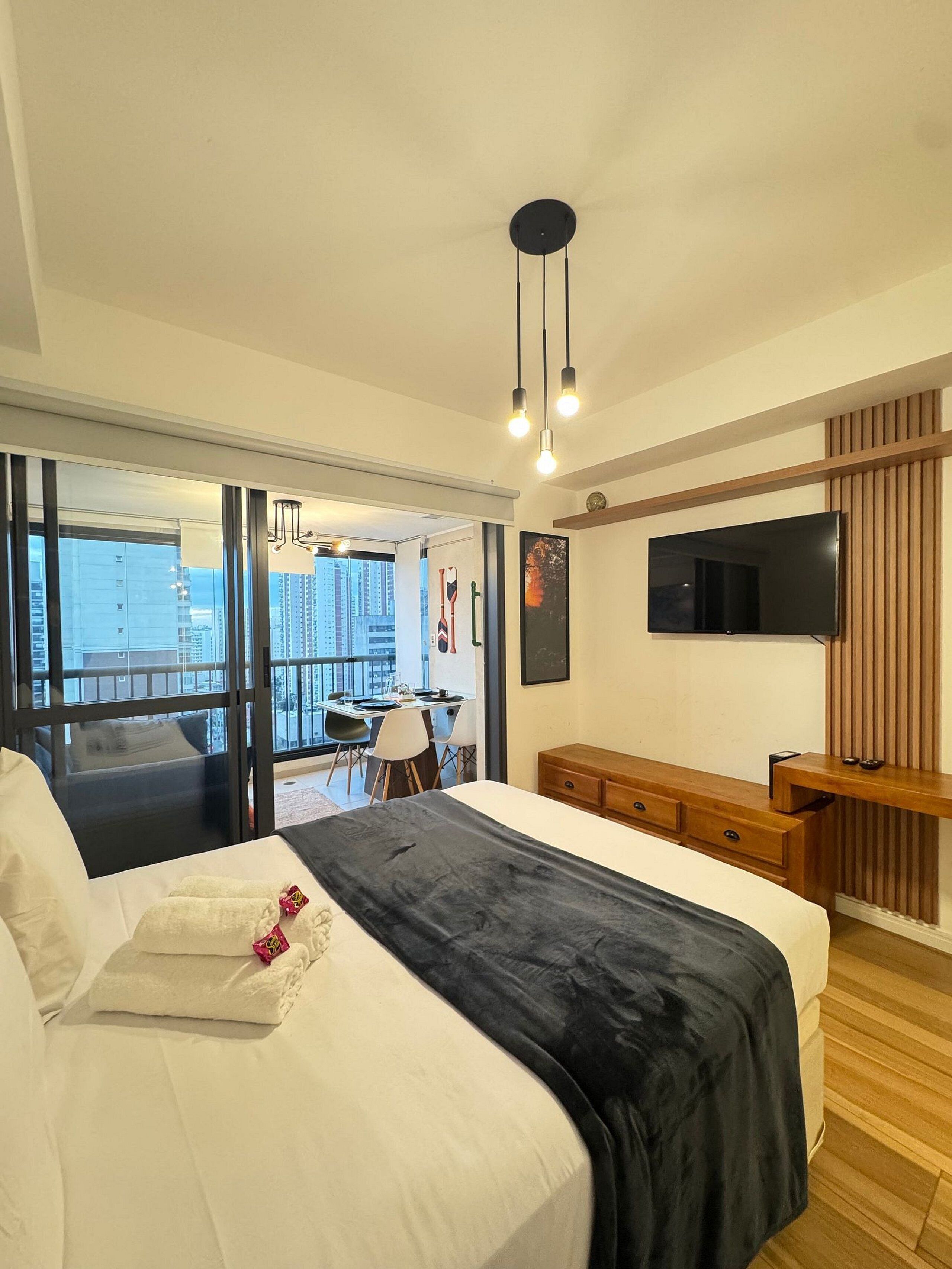 A modern hotel room with a large bed, a TV mounted on the wall, and a balcony with a view of the city.