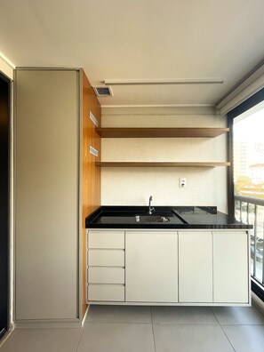 A modern kitchen with a black countertop, white cabinets, and a window providing a view of the outside. - Charmosos Studios no coração de Sampa (São Paulo)