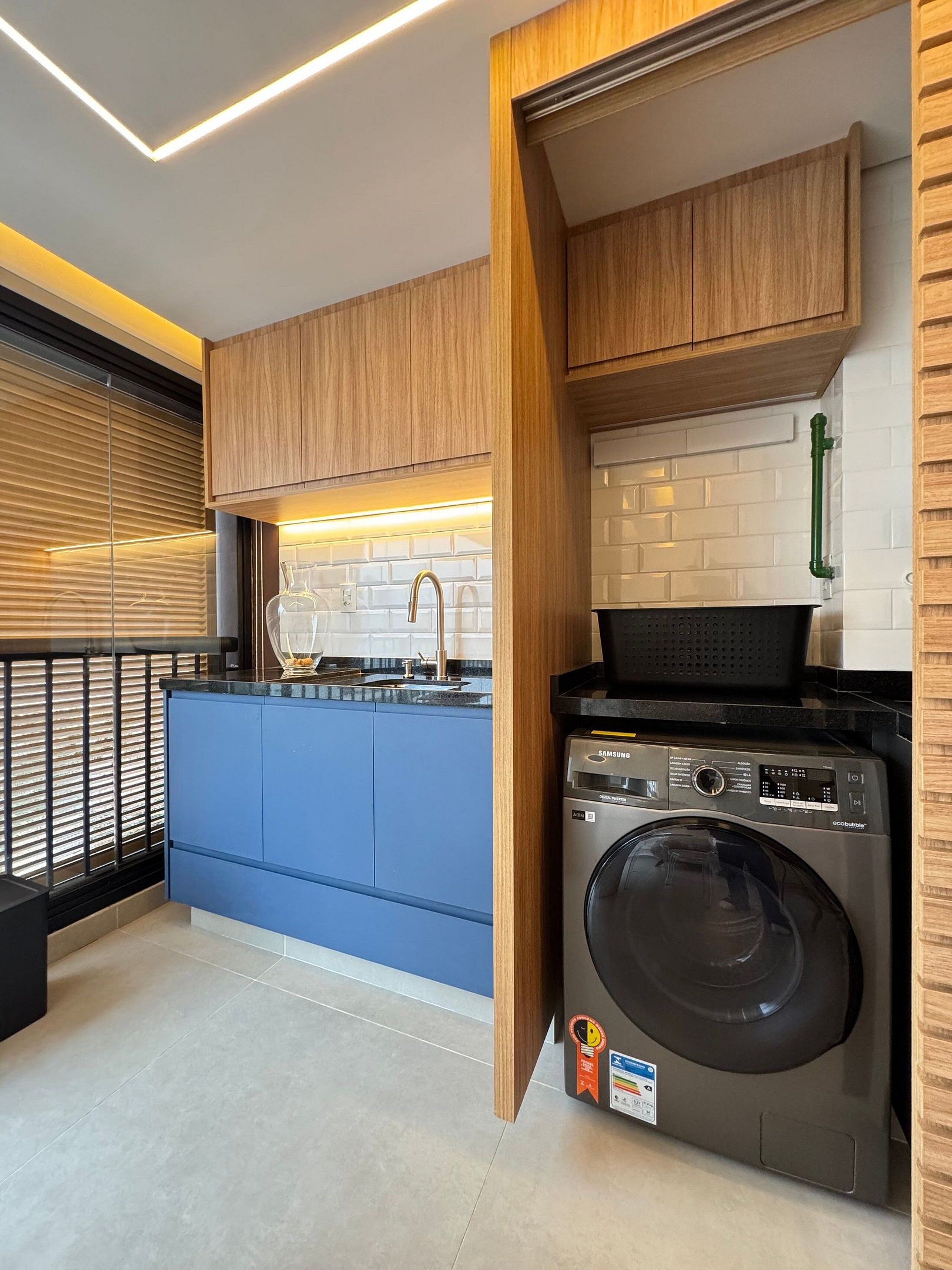 Une cuisine compacte avec des meubles de rangement en bois, un lave-linge encastré et un plan de travail bleu.