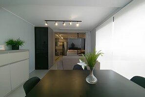 Ett modernt matområde med ett mörkt träbord, en vas med gröna växter och utsikt över ett kök och ett vardagsrum.