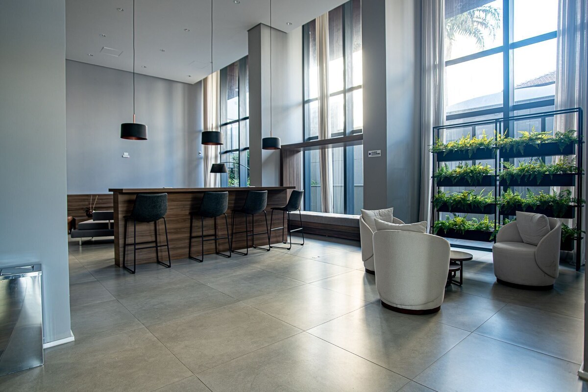 Una cocina moderna con barra, ventanas amplias y zona de estar con sofá y sillones blancos.