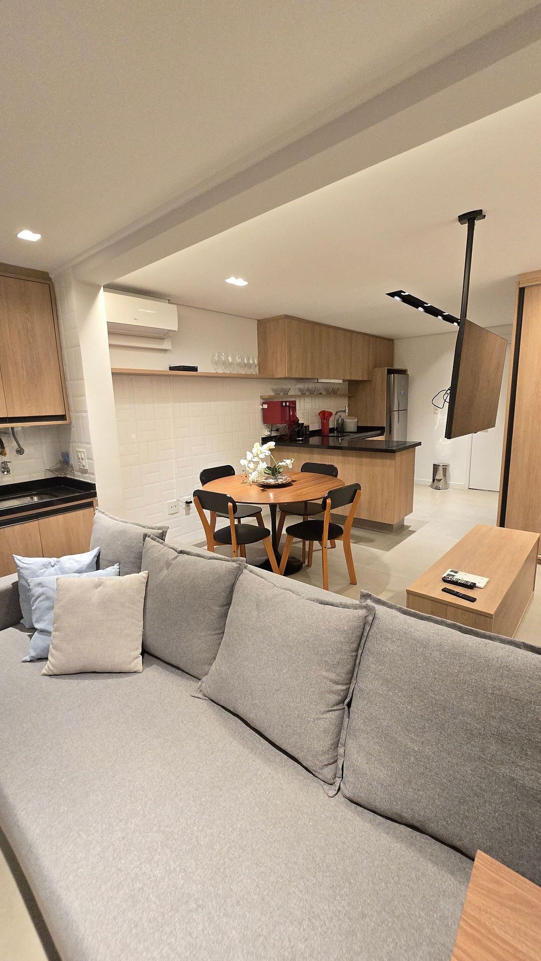 A modern living room with a grey sofa, a dining table with chairs, and a kitchen in the background.