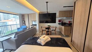 Ett modernt hotellrum med balkong, soffa, matbord och ett litet kök.