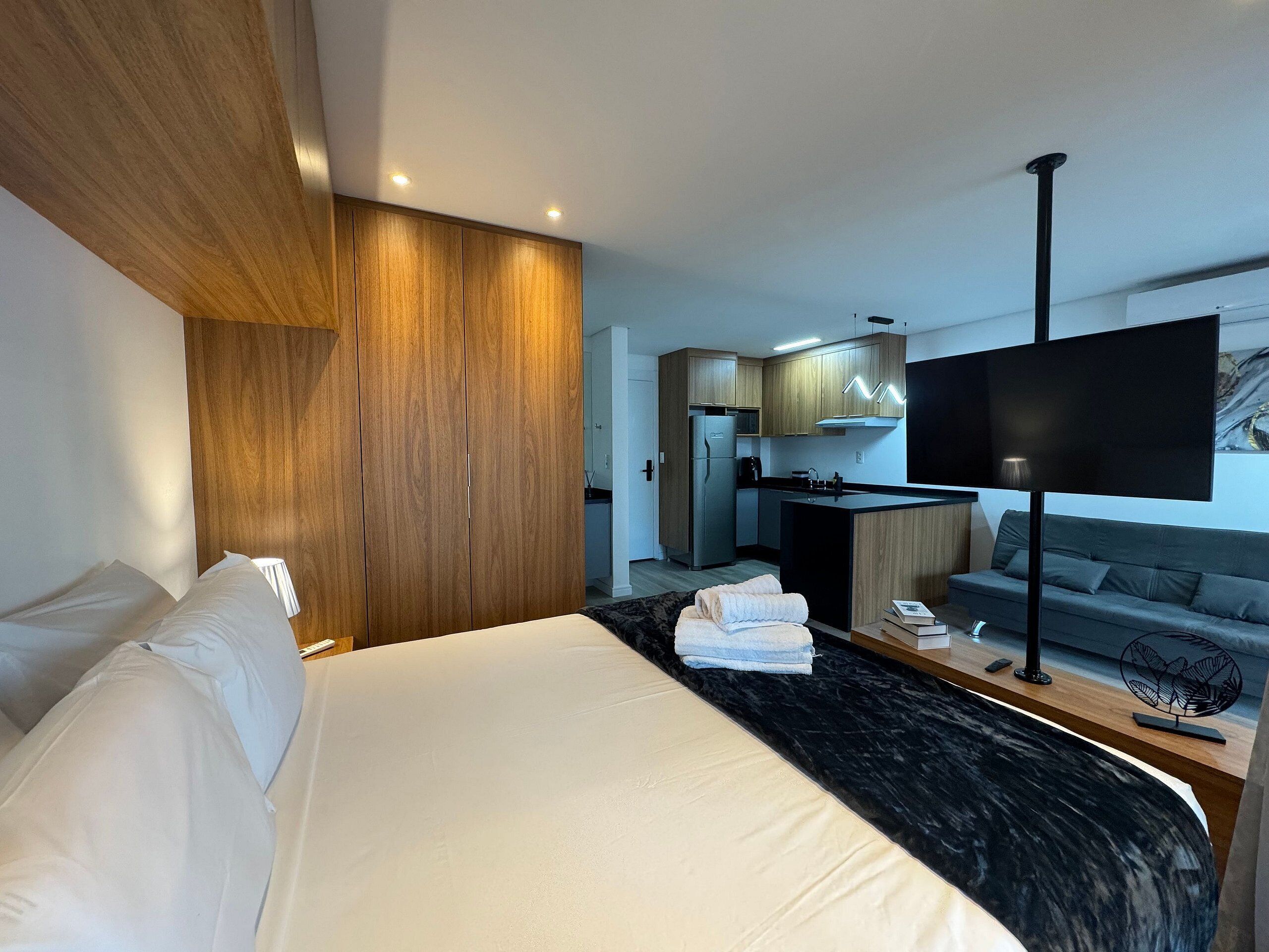 Una camera d'albergo moderna con un letto grande, un armadio in legno, un angolo cottura e una televisione a schermo piatto.