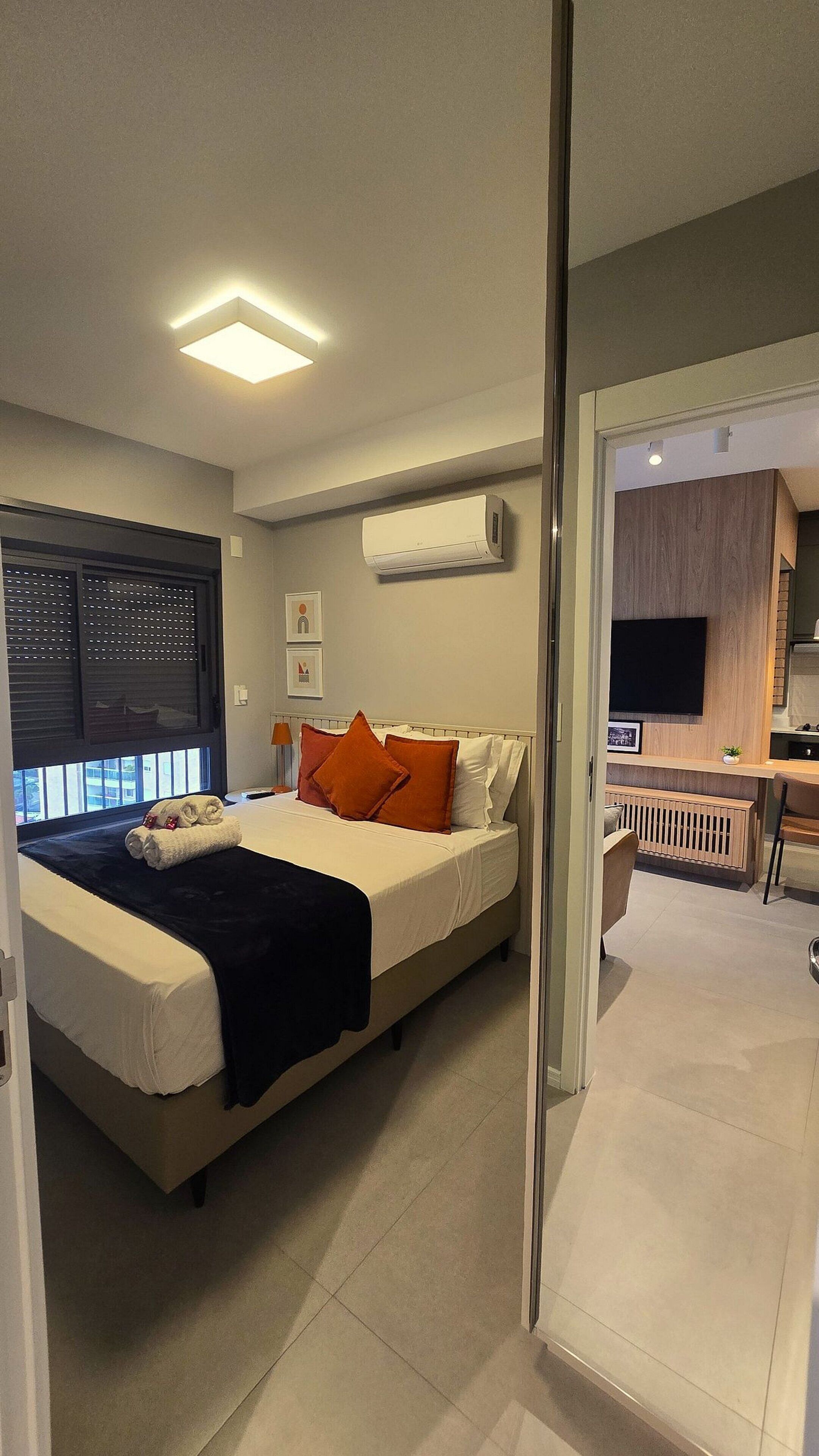 A modern bedroom with a bed, a TV, and an air conditioning unit.