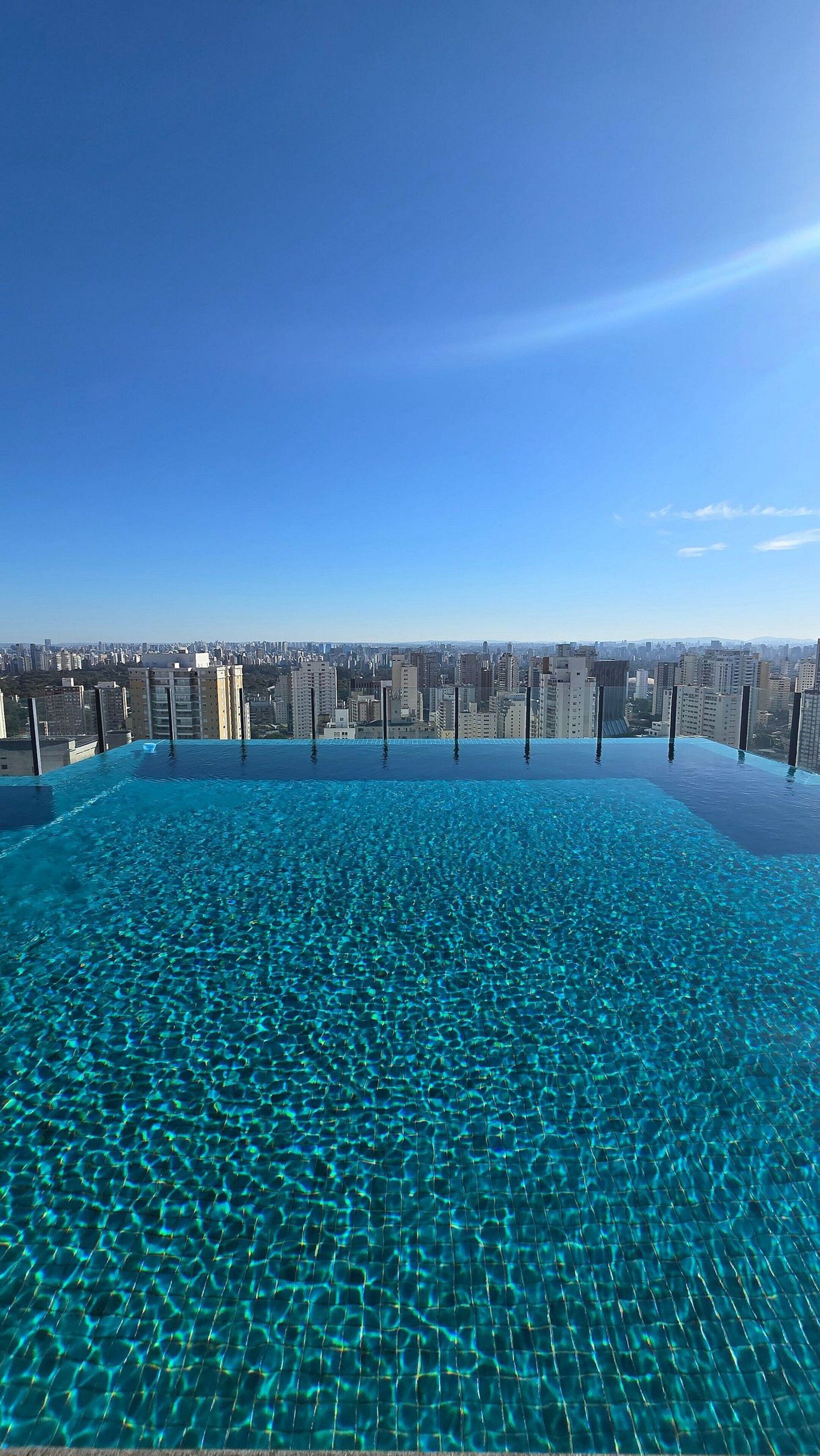 An infinity pool with clear blue water and a cityscape view in the background.