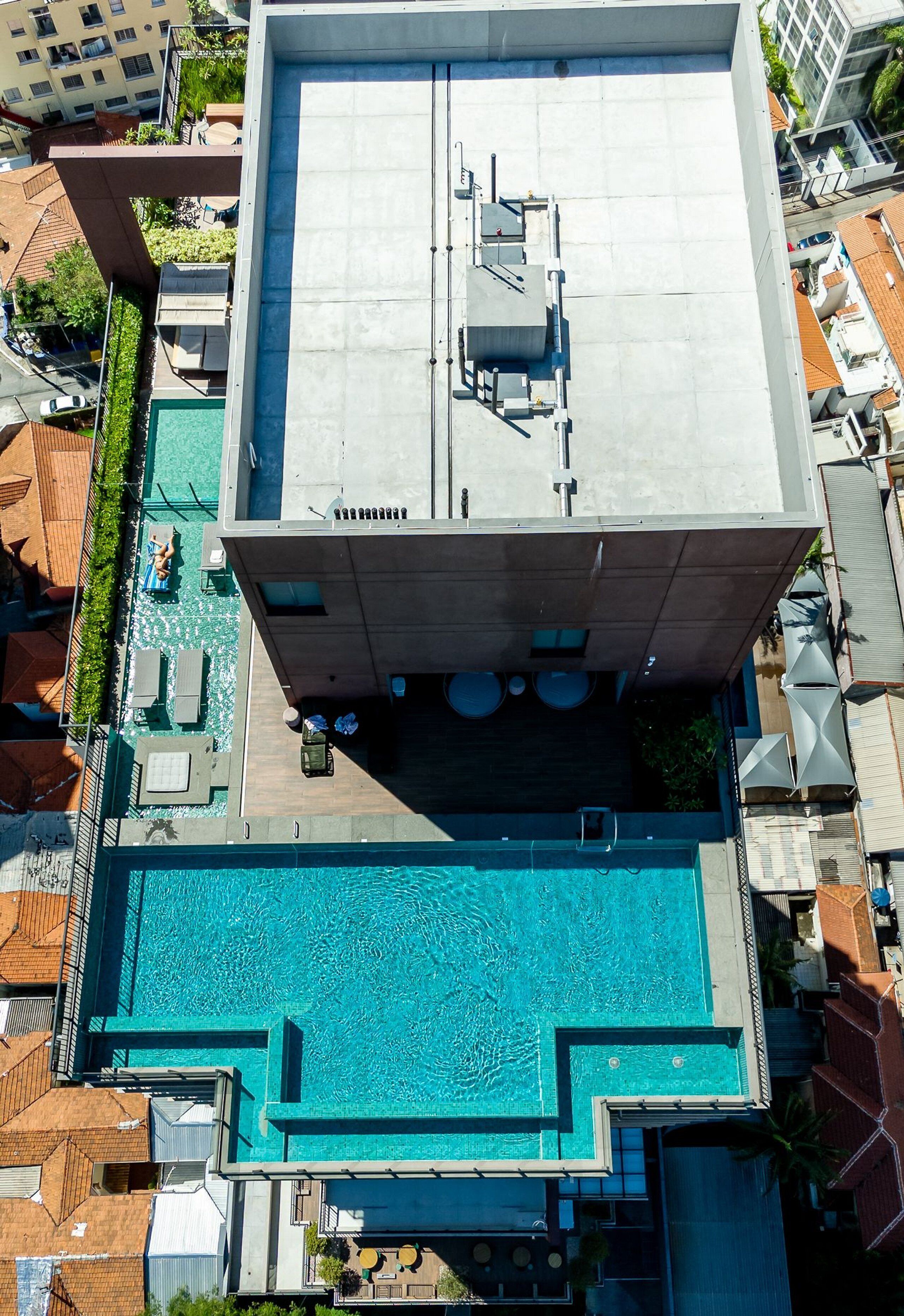 An aerial view of a building with a rooftop swimming pool, a covered outdoor area with seating, and a view of surrounding buildings.