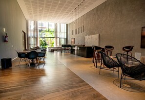 A spacious, modern hotel lobby with a wooden floor, a reception desk, and black wireframe chairs. - Charmosos Studios no coração de Sampa (São Paulo)