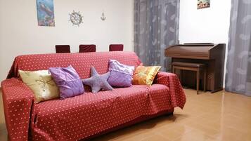 Un canapé rouge à pois et orné de motifs en forme de cœur, agrémenté de plusieurs coussins, d’une table d’appoint en bois et d’une décoration murale représentant un gouvernail de navire.