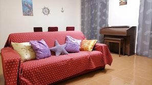 Un divano rosso con pois e motivi a cuore, arricchito da diversi cuscini, un tavolino in legno e una decorazione a forma di timone fissata al muro.