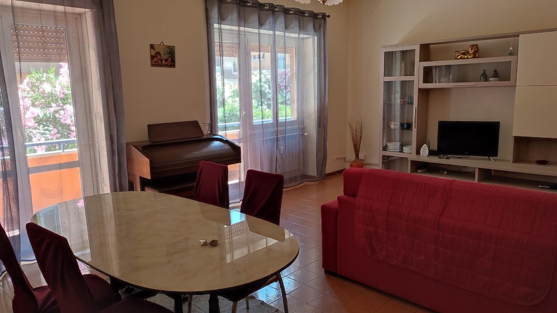 Un soggiorno con un pianoforte, un divano rosso, una TV su un mobile e un tavolo da pranzo con sedie.