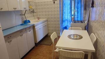 Una cucina compatta con mobili bianchi, un lavello e un tavolo con sedie.