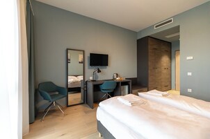 A modern hotel room with a bed, a desk, a chair, and a television.