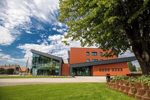 A modern building with a glass facade and a brick exterior, surrounded by a well-maintained lawn and a large tree.