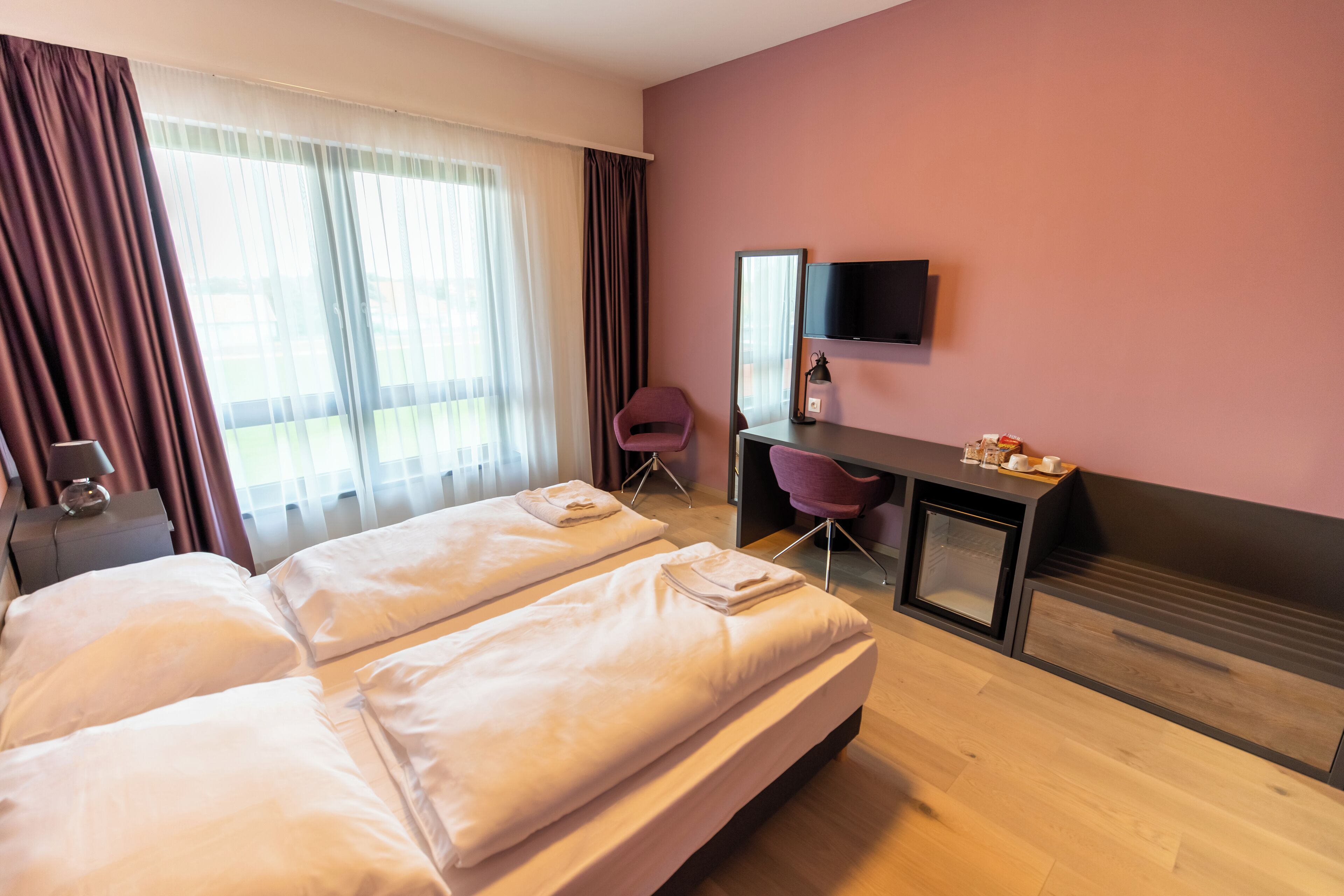A hotel room with two beds, a desk with a chair, a TV, and a window with curtains.