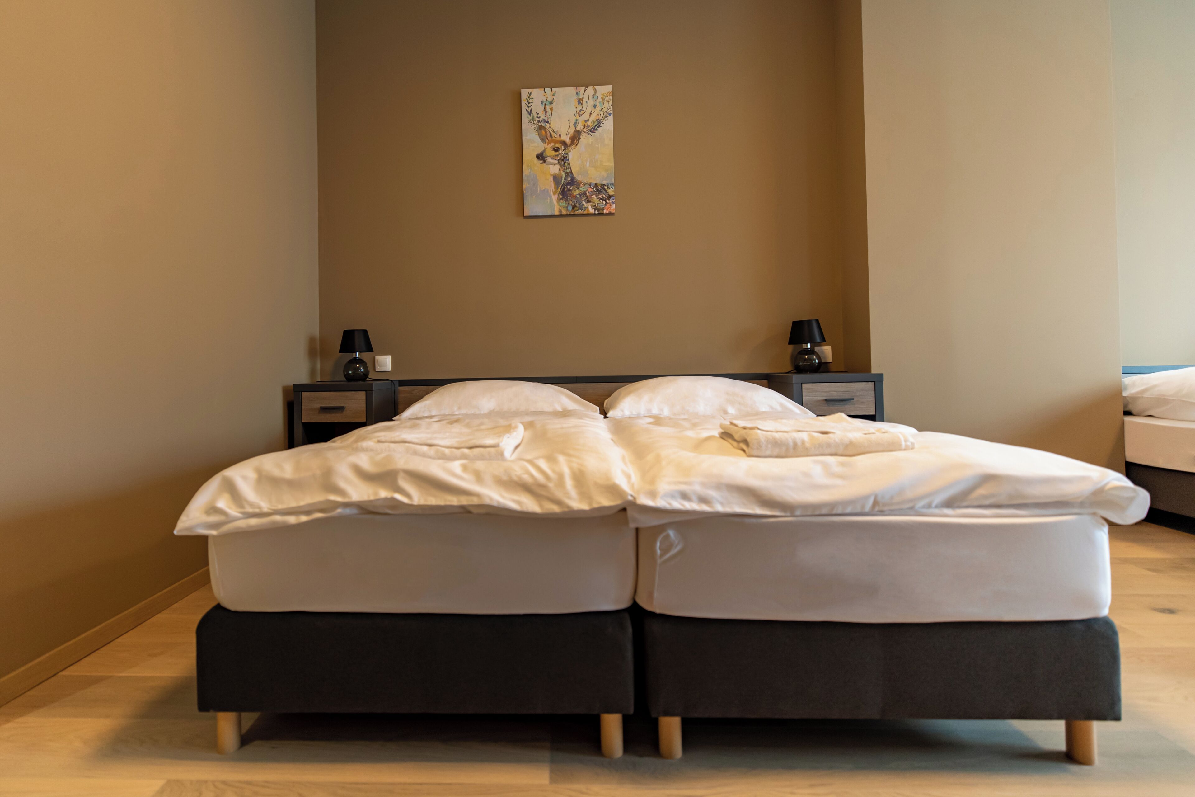 Una cama doble con ropa de cama blanca, dos mesitas de noche con lámparas y un cuadro en la pared.