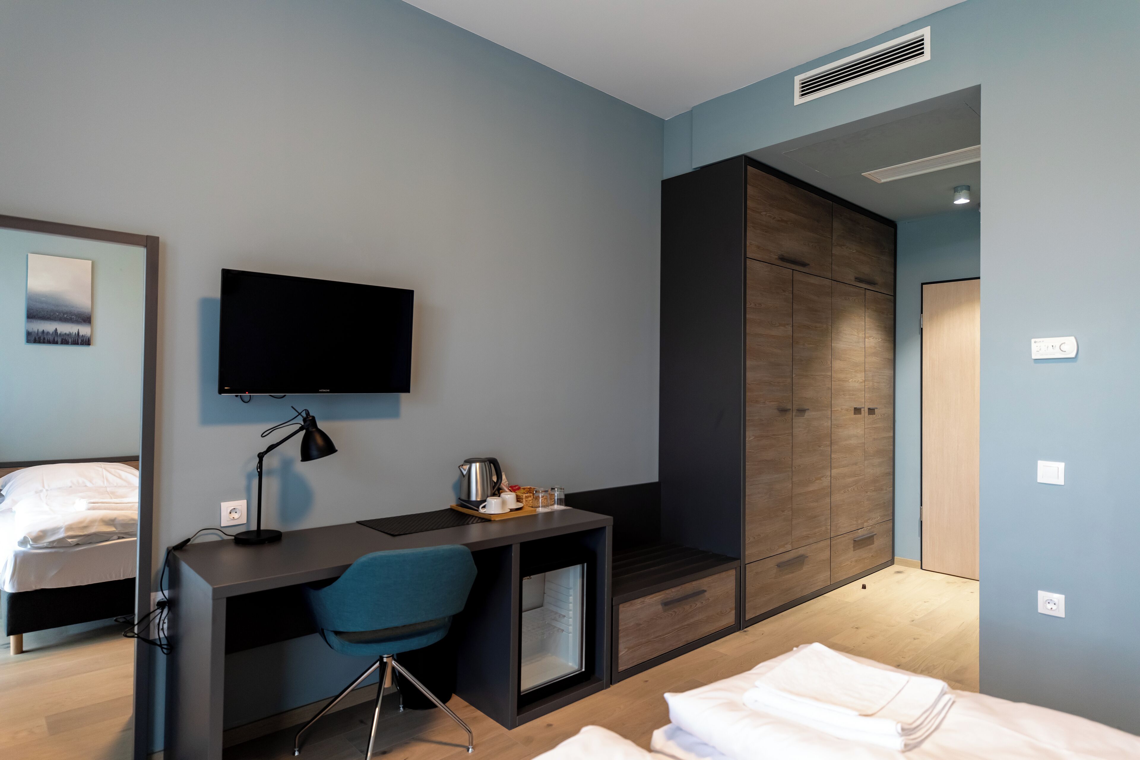 Una habitación de hotel moderna con cama, escritorio, silla, televisor y armario.