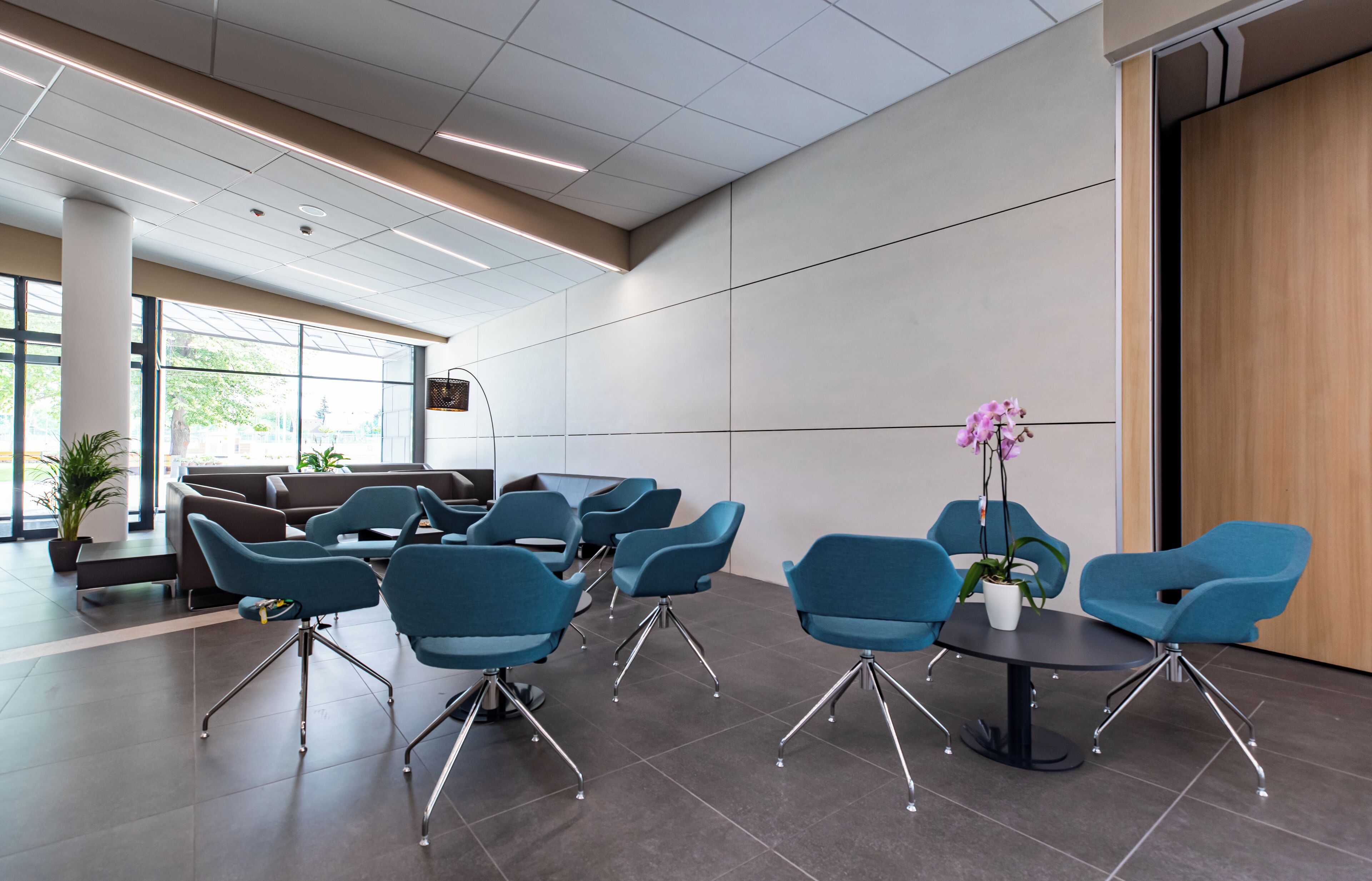 A modern waiting area with blue chairs, a round table, and potted plants.