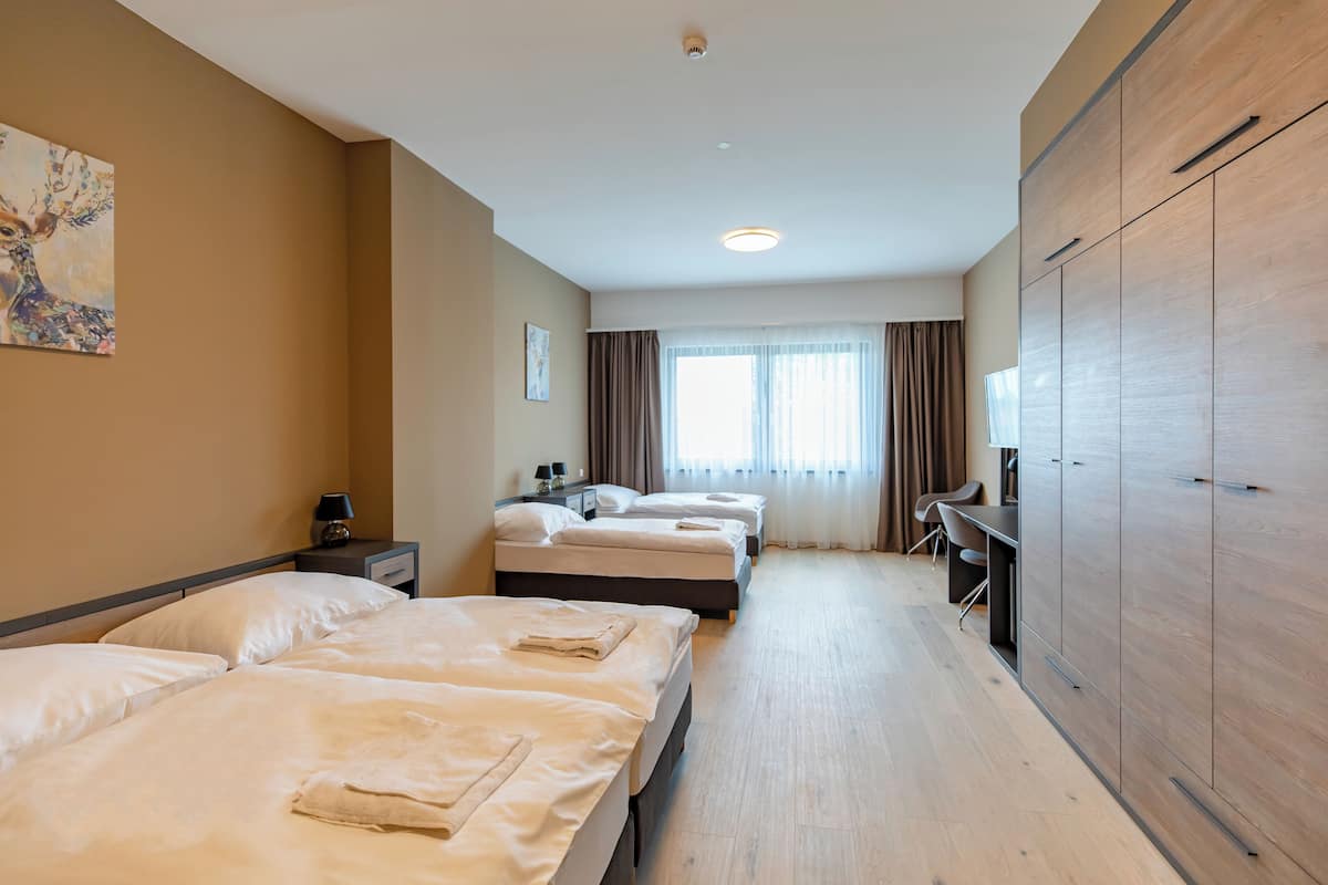 Une chambre d’hôtel avec trois lits, un bureau, une armoire et un tableau au mur.