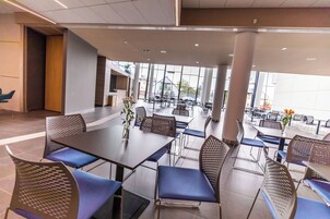 A modern dining area with tables and chairs, large windows, and a view of the outside.