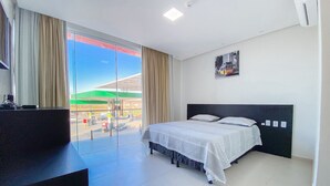 A hotel room with a bed, a desk, and a view of a gas station through a large window.