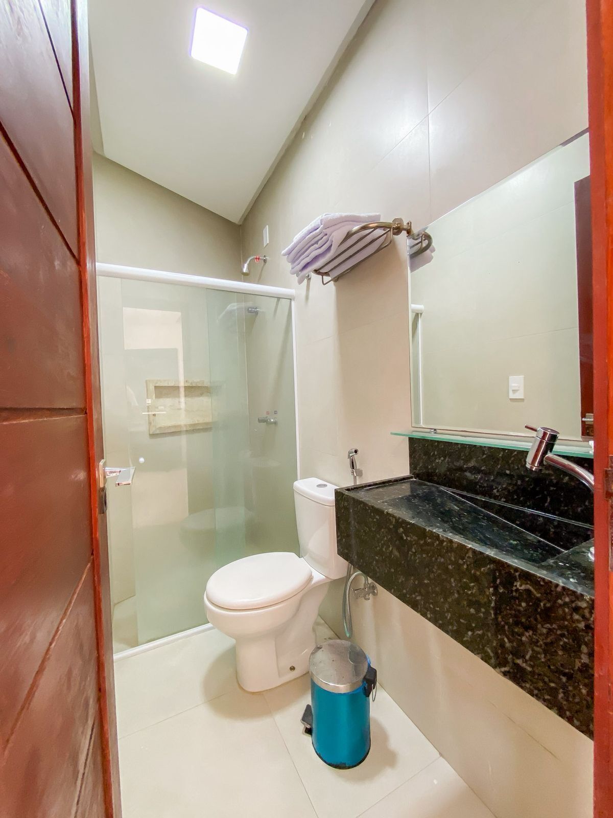 A bathroom with a glass shower enclosure, a white toilet, a blue bucket, and a marble countertop.
