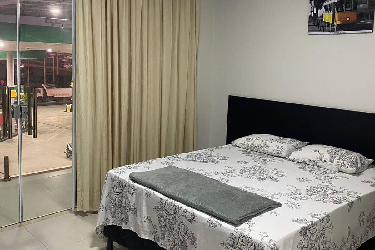 A hotel room with a bed, a view of a gas station through a glass door, and a painting on the wall.